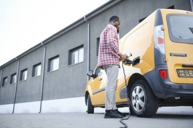 Afrikalı Amerikalı adam elektrikli arabasını şarj ediyor.