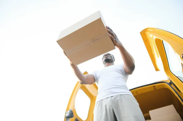 Low Angle View Of Loader Man Standing Near The Van Holding Cardboard Box.