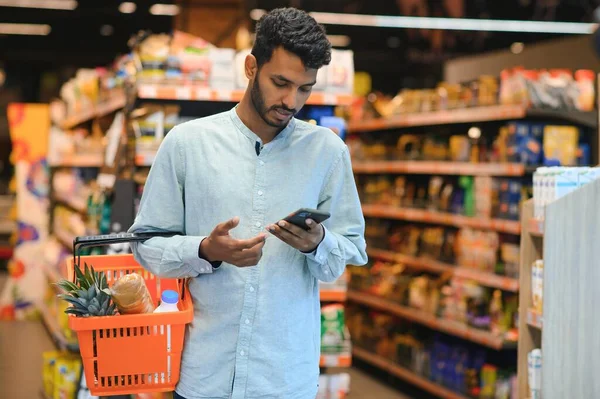 Young man using mobile phone while shopping at supermarket.