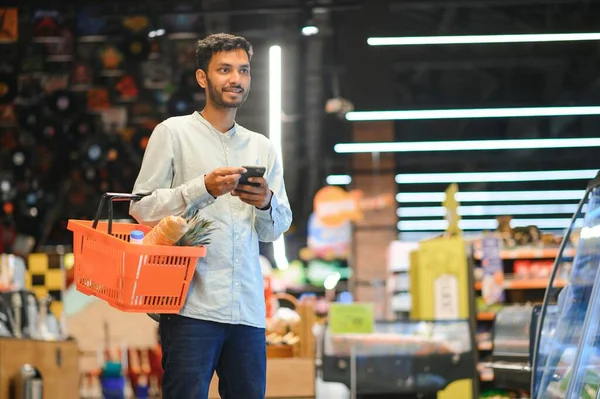 Young man using mobile phone while shopping at supermarket.