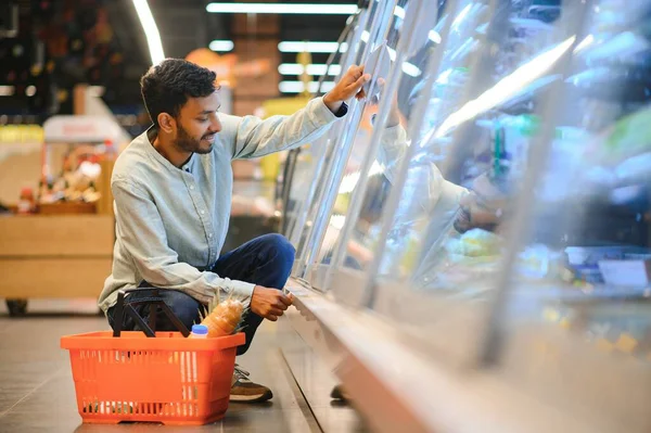 Portrait of handsome young Indian man standing at grocery shop or supermarket, Closeup. Selective Focus