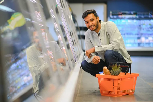Portrait of happy Indian man standing in front of the product counter in a grocery store. Man buying grocery for home in supermarket