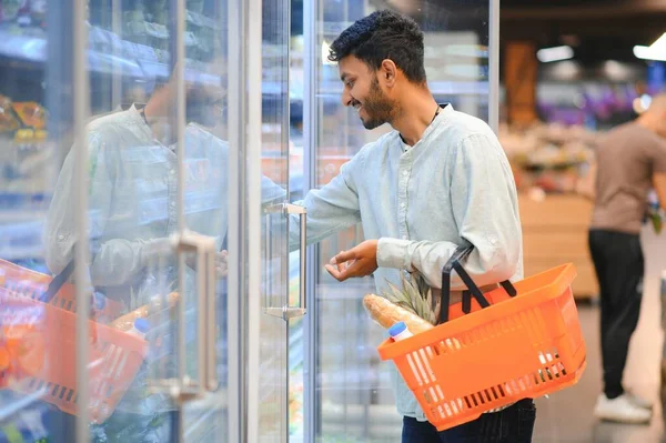 Portrait of happy Indian man standing in front of the product counter in a grocery store. Man buying grocery for home in supermarket