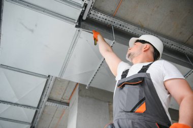 Erkek tamirci. Usta havalandırma borularının yanında. Binalar için havalandırma kurulumu. Kameraya geri dönen bir tamirci. Metal havalandırma boruları