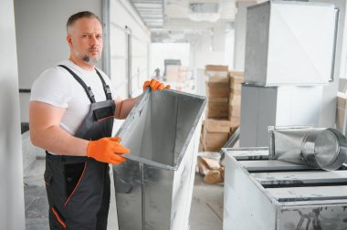 Erkek tamirci. Usta havalandırma borularının yanında. Binalar için havalandırma kurulumu. Kameraya geri dönen bir tamirci. Metal havalandırma boruları