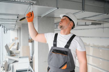 Adam içeride havalandırma sistemi kuruyor. Bir erkek işçi yeni bir ofis binasına havalandırma boruları yerleştiriyor.