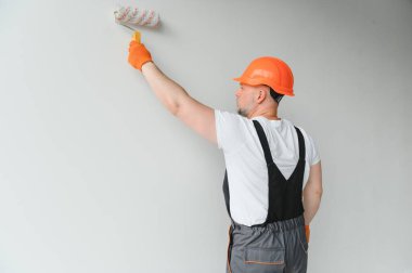 Boyacı boya silindiri kullanıyor ve beyaz arkaplanda izole edilmiş bir duvar boyuyor.