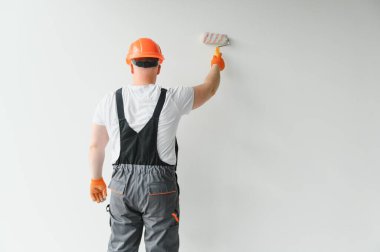 Boyacı boya silindiri kullanıyor ve beyaz arkaplanda izole edilmiş bir duvar boyuyor.