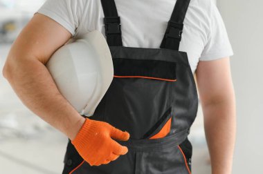 Bir inşaat işçisinin elinde proje belgeleri ve şapkasını tutarken.