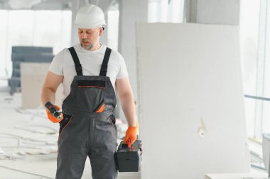 İnşaat alanındaki aletlerle birlikte koruyucu kasklı, işçi üniformalı bir müteahhit portresi..