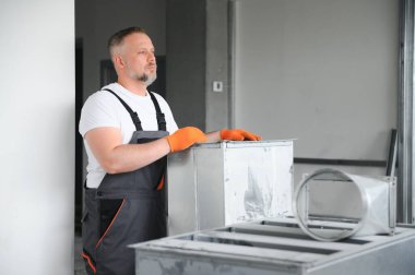 Adam içeride havalandırma sistemi kuruyor. Bir erkek işçi yeni bir ofis binasına havalandırma boruları yerleştiriyor.