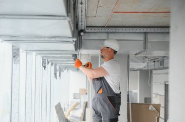 Erkek tamirci. Usta havalandırma borularının yanında. Binalar için havalandırma kurulumu. Kameraya geri dönen bir tamirci. Metal havalandırma boruları