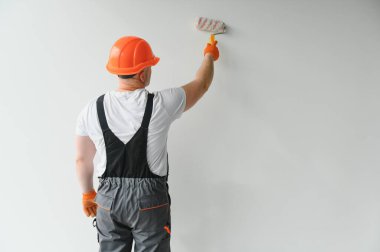 Boyacı evin duvarını boyuyor, boya silindiri ve beyaz boyayla. Evdeki oda tadilatı