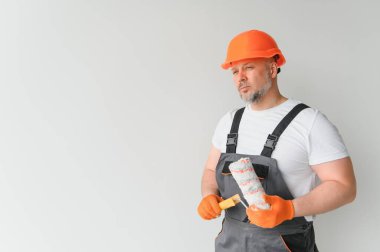 Boyacı boya silindiri kullanıyor ve beyaz arkaplanda izole edilmiş bir duvar boyuyor.