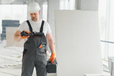 İnşaat alanındaki aletlerle birlikte koruyucu kasklı, işçi üniformalı bir müteahhit portresi..