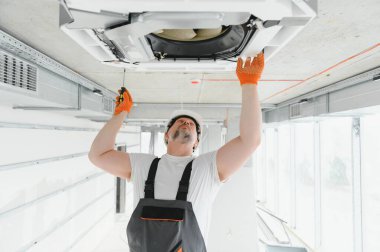 İşçi tavan havalandırma ünitesini tamir ediyor.