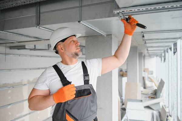 Man setting up ventilation system indoors. A male worker installs air ventilation pipes in a new office building