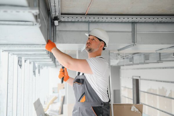 Man setting up ventilation system indoors. A male worker installs air ventilation pipes in a new office building