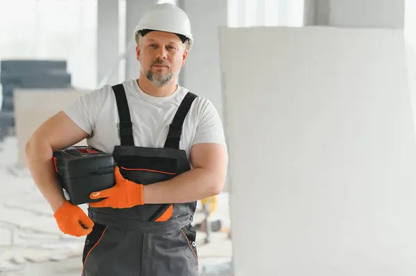 A man with a beard in a helmet and work clothes. Portrait of a worker in workwear with copy space