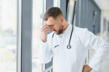 Üzgün doktor hastane koridorunda duvara yaslanıyor.