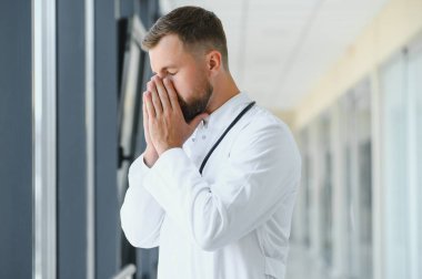 Üzgün doktor hastane koridorunda duvara yaslanıyor.