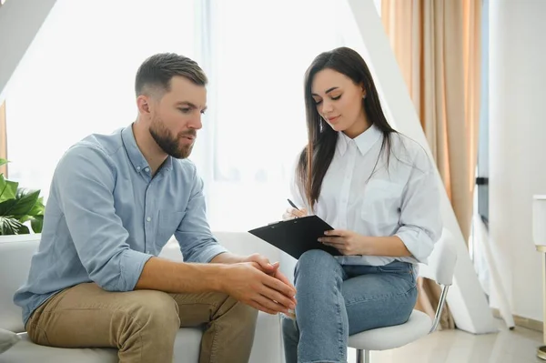 stock image Psychologist talking with patient on therapy session. Depressed man speaking to a therapist while she is taking notes.