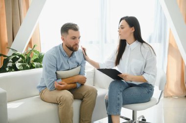 Psychologist talking with patient on therapy session. Depressed man speaking to a therapist while she is taking notes.