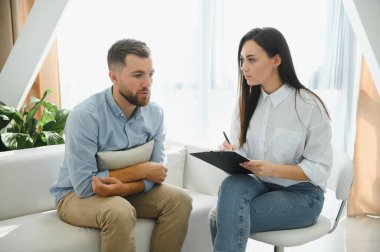 Psychologist talking with patient on therapy session. Depressed man speaking to a therapist while she is taking notes.