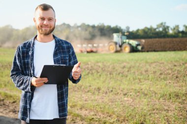 Agronomist tarlada yetişen soya fasulyesi ekinlerini inceliyor. Tarım üretim konsepti. Genç tarımcı tarlada soya fasulyesi mahsulünü inceliyor. Soya tarlasında çiftçi