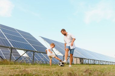 Baba ve oğlu güneş panellerinin yanında futbol oynarken eğleniyor. Yeşil enerji kavramı.
