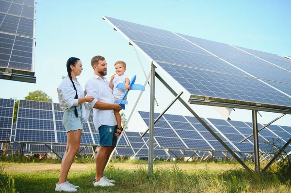 stock image Young family with a small child in her arms on a background of solar panels. A man and a woman look at each other with love. Solar energy concept