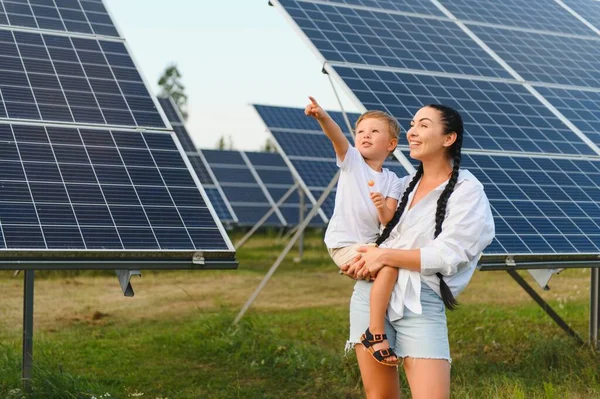 A child and her mother in the fresh open air, beside solar panels on a sunny day at a farm.