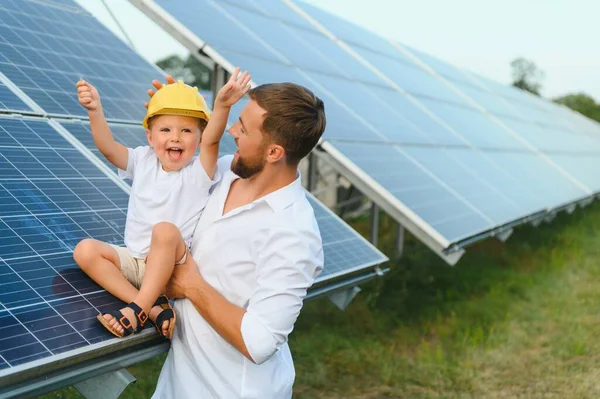 Mutlu baba ve küçük oğlu güneş panellerinin yanında yürüyorlar. Yeşil enerji kavramı