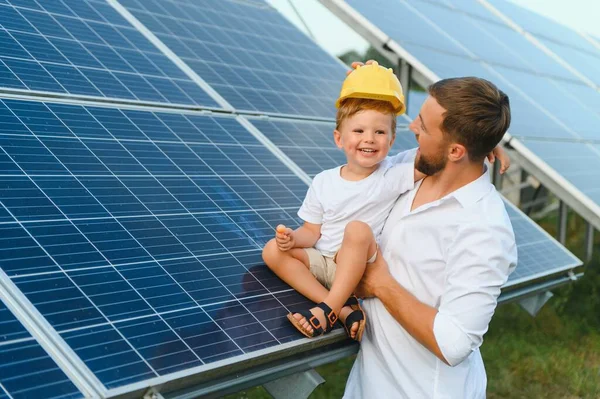 Mutlu baba ve küçük oğlu güneş panellerinin yanında yürüyorlar. Yeşil enerji kavramı