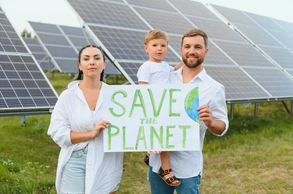 A family of activists and nature defenders stands with a poster about the protection of nature against the background of solar panels. The concept of green energy and nature protection