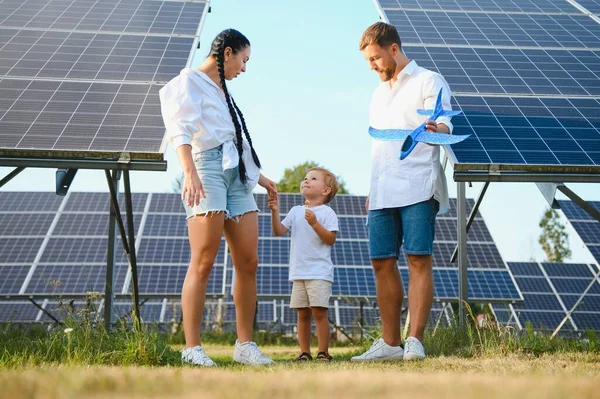 Young family of three is crouching near photovoltaic solar panel, little boy and parents. modern family concept. The concept of green energy.