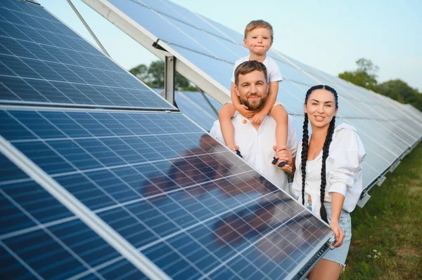 Üç kişilik genç aile fotovoltaik güneş panelinin yanında çömeliyor, küçük çocuk ve ebeveynler. Modern aile kavramı. Yeşil enerji kavramı.