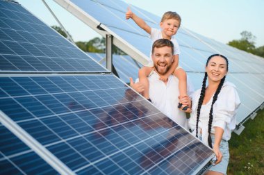 Kollarında güneş panellerinin arka planında küçük bir çocuk olan genç bir aile. Bir erkek ve bir kadın birbirlerine sevgiyle bakarlar. Güneş enerjisi kavramı