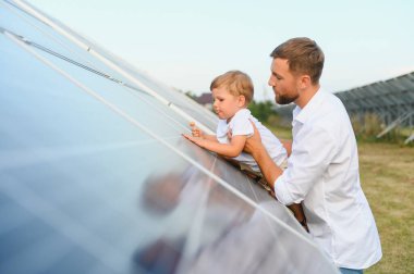 Man showing little child the solar panels during sunny day. Father presenting to his kid modern energy resource. Little steps to alternative energy