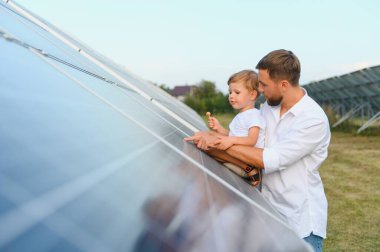 Mutlu baba ve küçük oğlu güneş panellerinin yanında yürüyorlar. Yeşil enerji kavramı