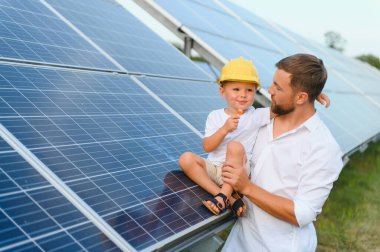 Mutlu baba ve küçük oğlu güneş panellerinin yanında yürüyorlar. Yeşil enerji kavramı