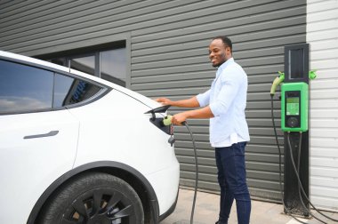 Man Plugging In Electric Car Outside Office In Car Park Charging.