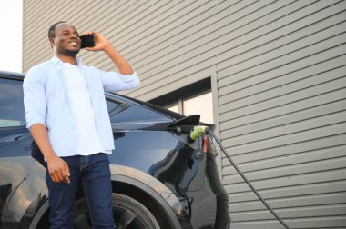 Afrikalı Amerikalı adam elektrikli arabasını şarj ediyor.