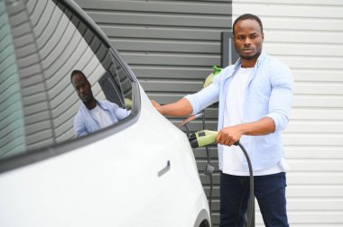 Afrikalı Amerikalı adam elektrikli arabasını şarj ediyor.