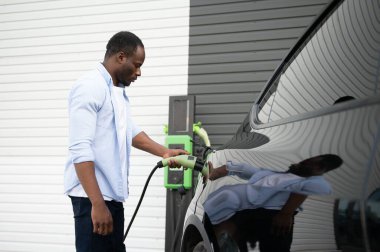 Ciddi bir Afrikalı elinde kabloyla lüks elektrikli arabanın yanında duruyor.