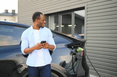 Afrikalı Amerikalı adam elektrikli arabasını şarj ediyor.