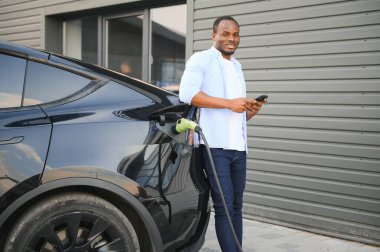 Afrikalı Amerikalı adam elektrikli arabasını şarj ediyor.