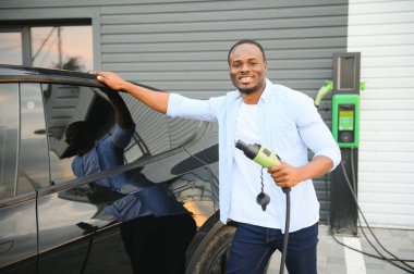 Afrikalı Amerikalı adam elektrikli arabasını şarj ediyor.
