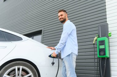 Şık bir adam elektrikli araba şarj prizine takar..