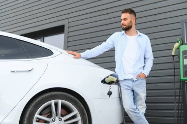 Bir adam elektrikli arabayı şarj eder..